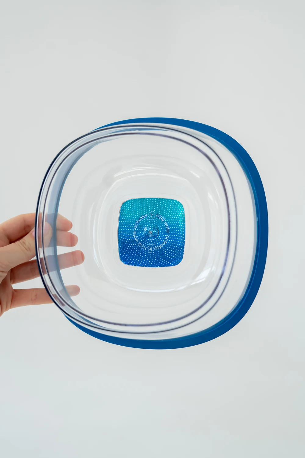 The real MOLECULE bowl held in one hand, showing its rounded-square shape and transparent construction
